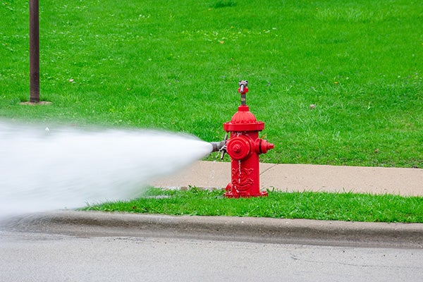Red fire hydrant being flushed, high pressure water spraying.